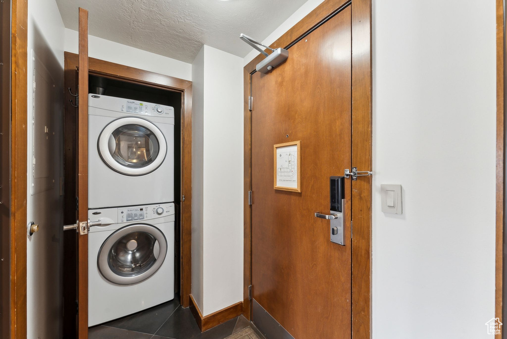 Clothes washing area with stacked washer / drying machine, tile patterned floors, and baseboards