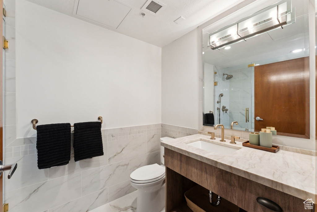 Bathroom with a shower, toilet, vanity, tile walls, and wainscoting