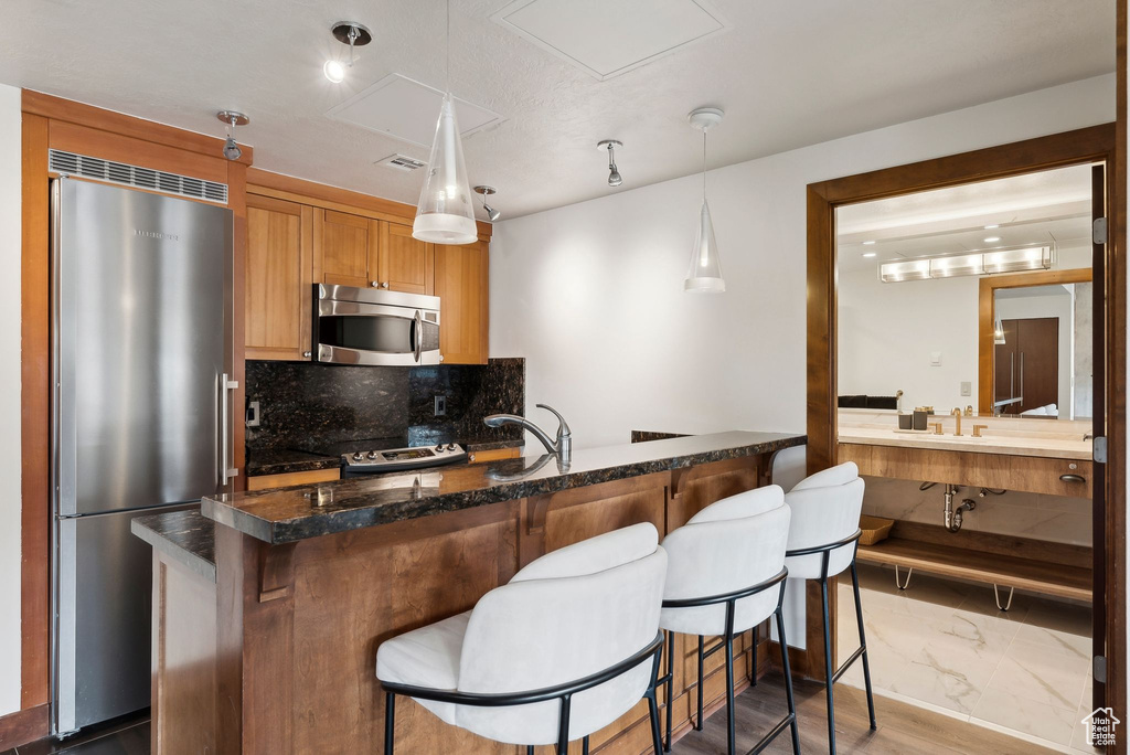 Kitchen featuring stainless steel appliances, decorative backsplash, a breakfast bar, pendant lighting, and dark stone countertops