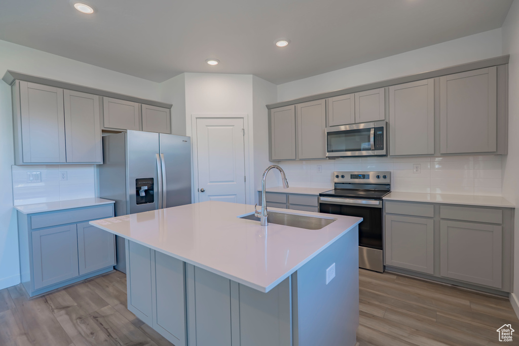 Kitchen with appliances with stainless steel finishes, gray cabinets, a sink, light wood-type flooring, and recessed lighting