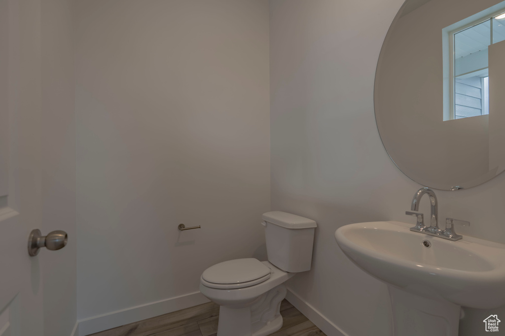 Bathroom featuring baseboards, toilet, a sink, and wood finished floors