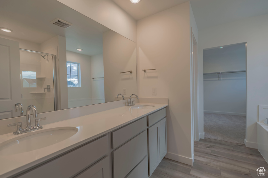 Full bath with a stall shower, double vanity, wood finished floors, a spacious closet, and a bathtub