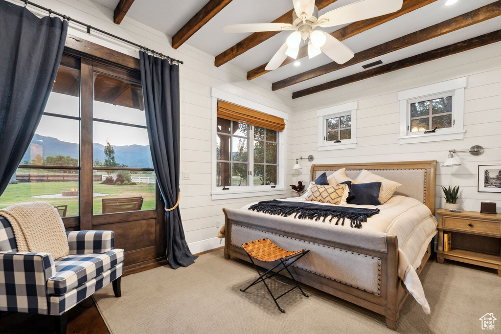 Bedroom with beamed ceiling, wooden walls, a mountain view, light carpet, and ceiling fan