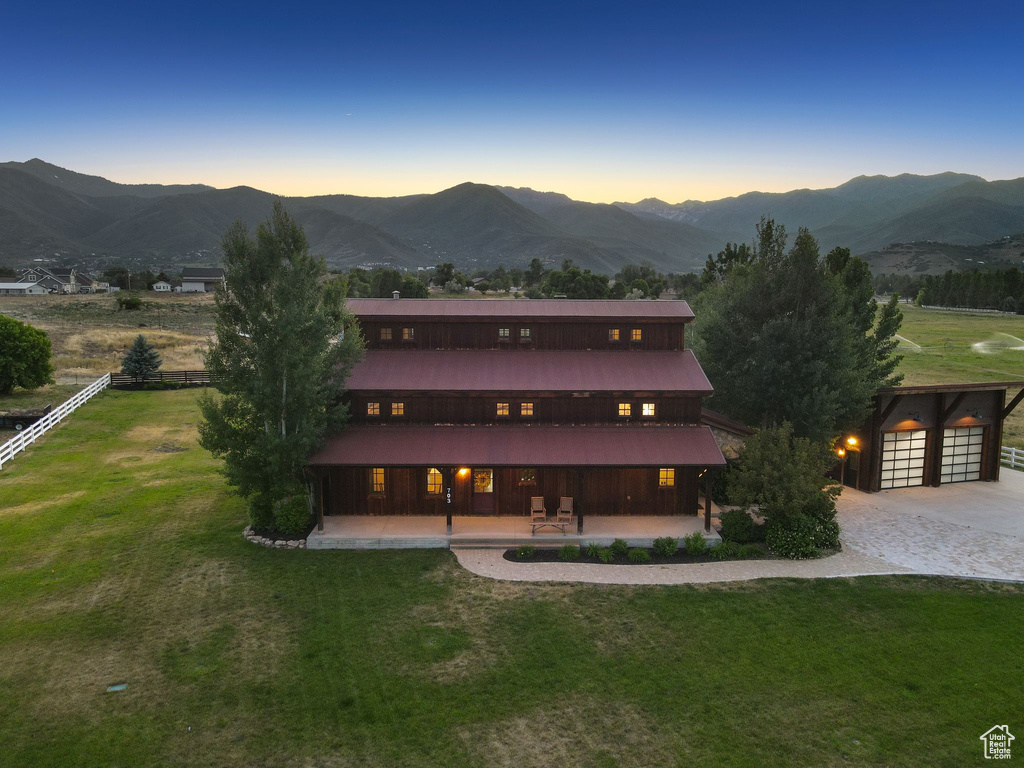 Back of property at dusk featuring a mountain view, a lawn, driveway, and an outdoor structure