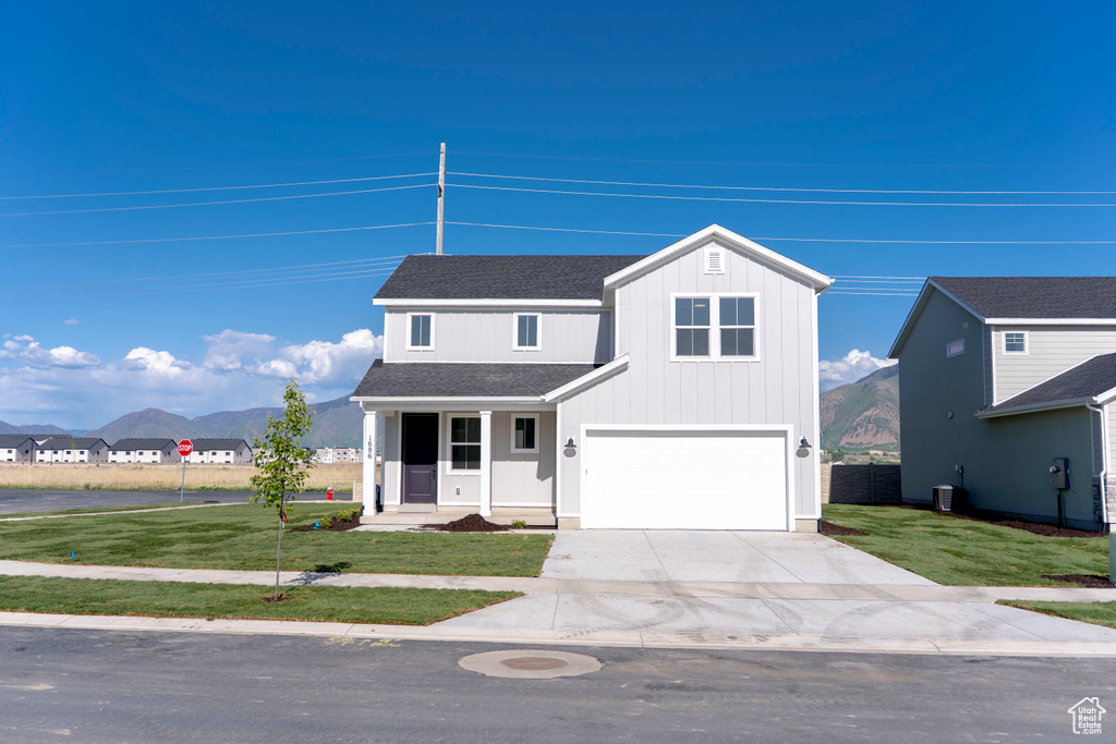Traditional-style home featuring concrete driveway, a front yard, a garage, roof with shingles, and a mountain view