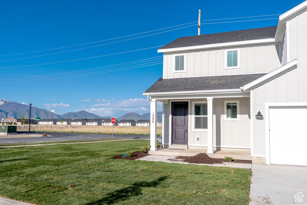 View of front of home featuring a shingled roof, a mountain view, a front lawn, a porch, and a garage