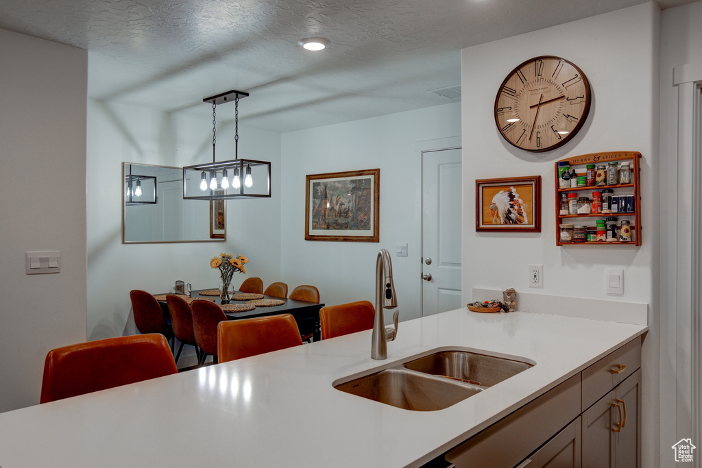 Kitchen with light countertops, a sink, hanging light fixtures, and a textured ceiling