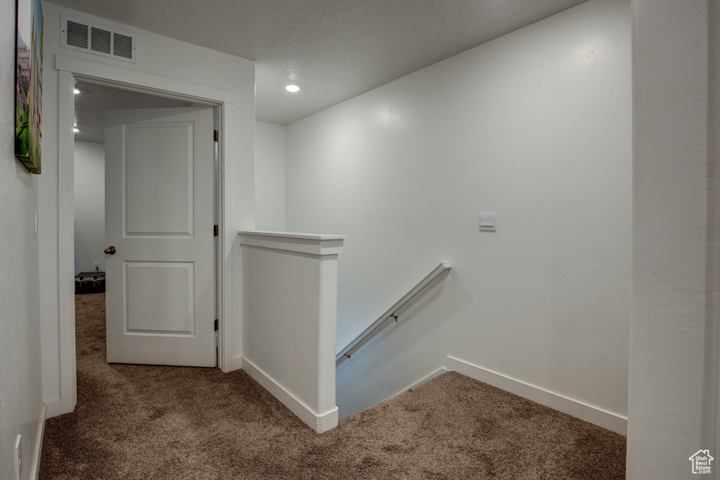 Hallway with carpet, an upstairs landing, visible vents, and baseboards