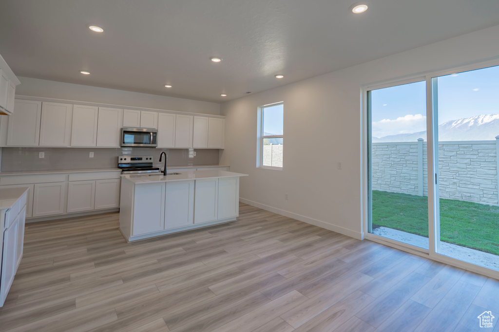 Kitchen featuring appliances with stainless steel finishes, light countertops, white cabinets, light wood-style flooring, and recessed lighting