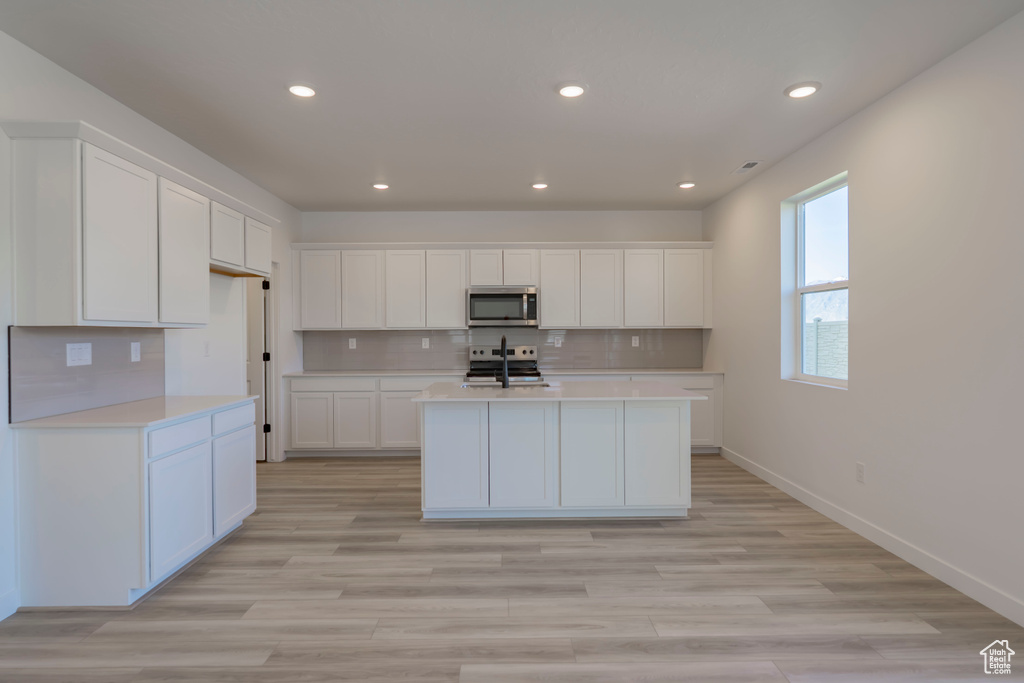 Kitchen featuring stainless steel appliances, light countertops, recessed lighting, white cabinets, and tasteful backsplash