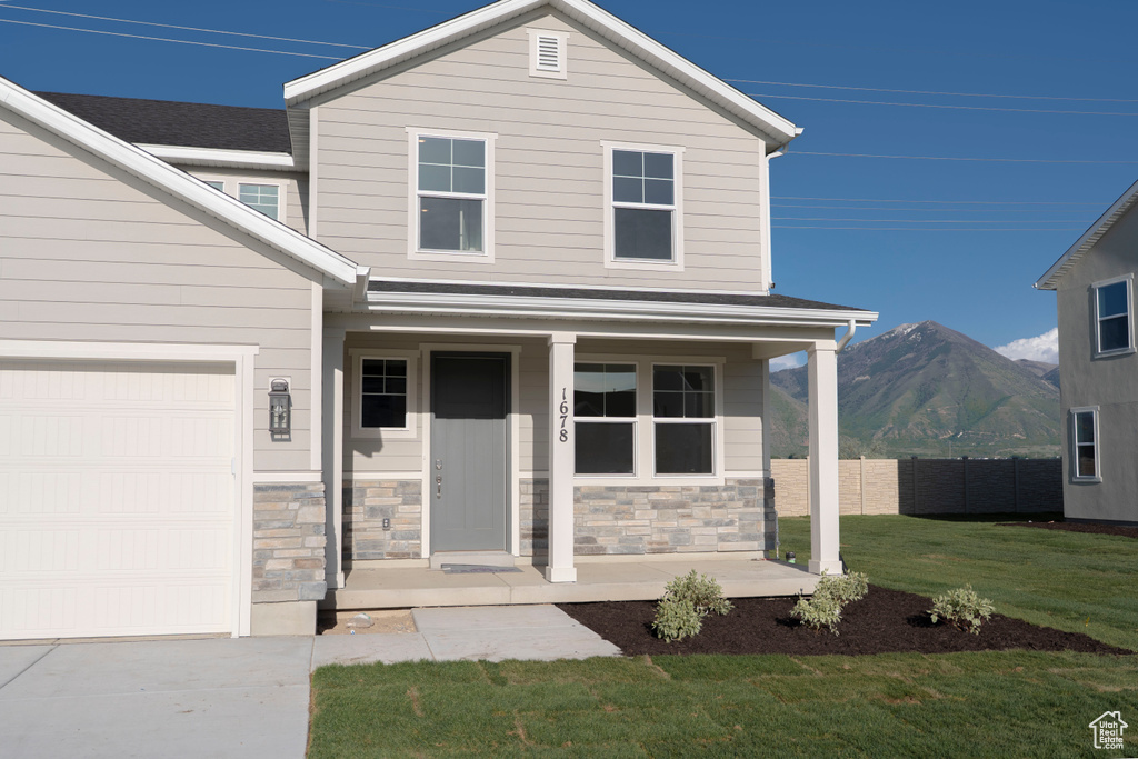 View of front facade with covered porch, a mountain view, a garage, stone siding, and driveway