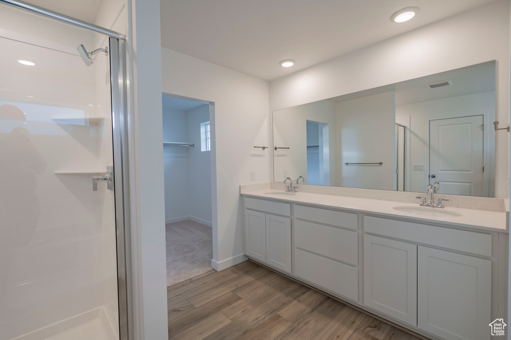 Full bath with a shower stall, wood finished floors, double vanity, a walk in closet, and baseboards