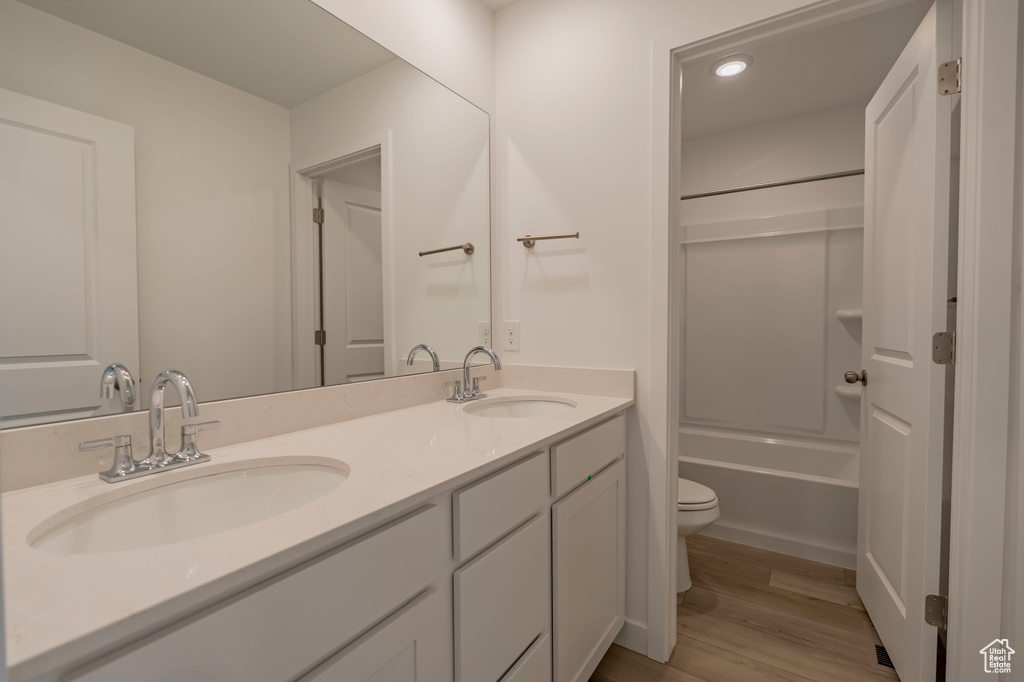 Bathroom with toilet, wood finished floors, double vanity, washtub / shower combination, and recessed lighting