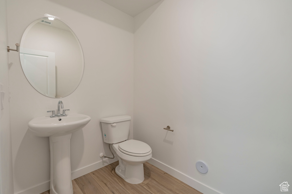 Half bathroom with wood finished floors, baseboards, toilet, and a sink