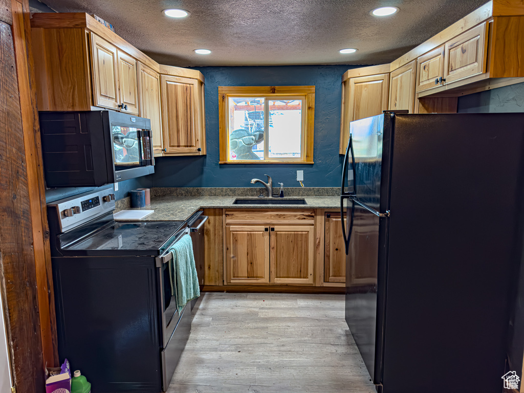 Kitchen with light wood-type flooring, sink, a textured ceiling, and black appliances