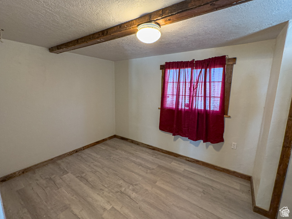 Empty room with beamed ceiling, wood-type flooring, and a textured ceiling