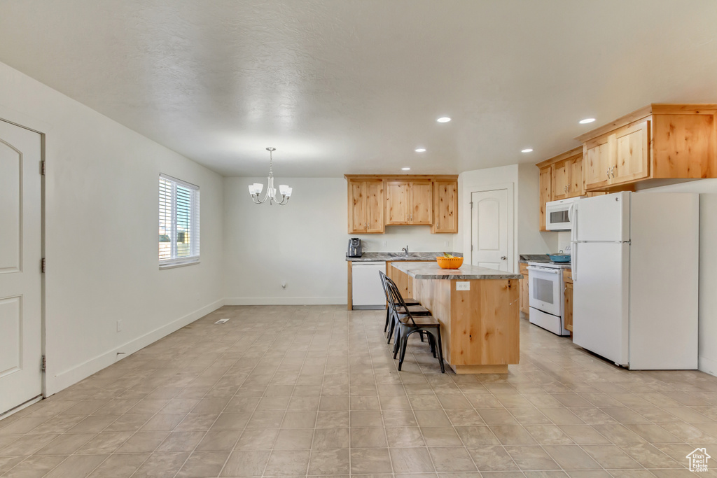 Kitchen with a breakfast bar, light brown cabinetry, a kitchen island, white appliances, and baseboards