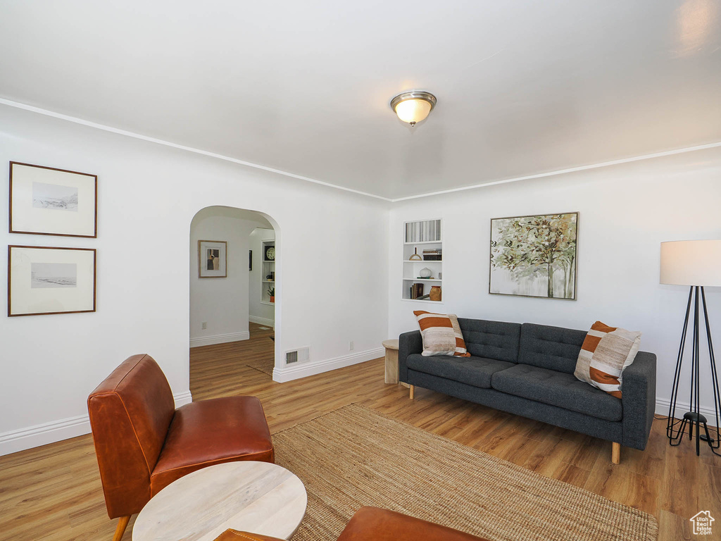 Living room with arched walkways, built in shelves, visible vents, baseboards, and light wood-style floors