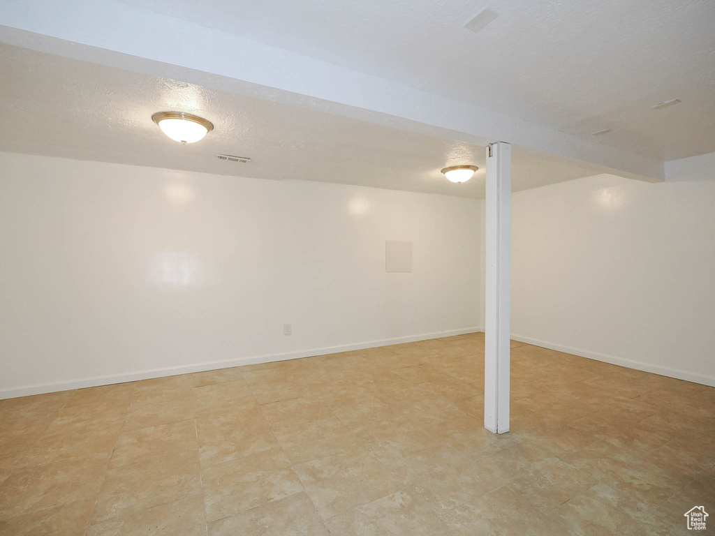 Finished basement featuring a textured ceiling, visible vents, and baseboards