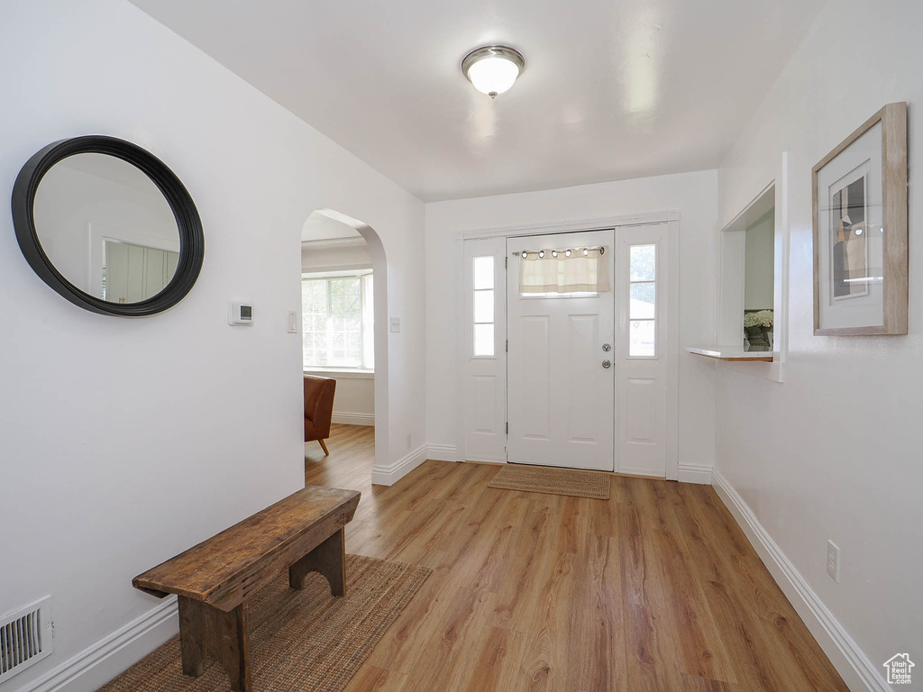 Entryway with arched walkways, visible vents, light wood-style flooring, and baseboards