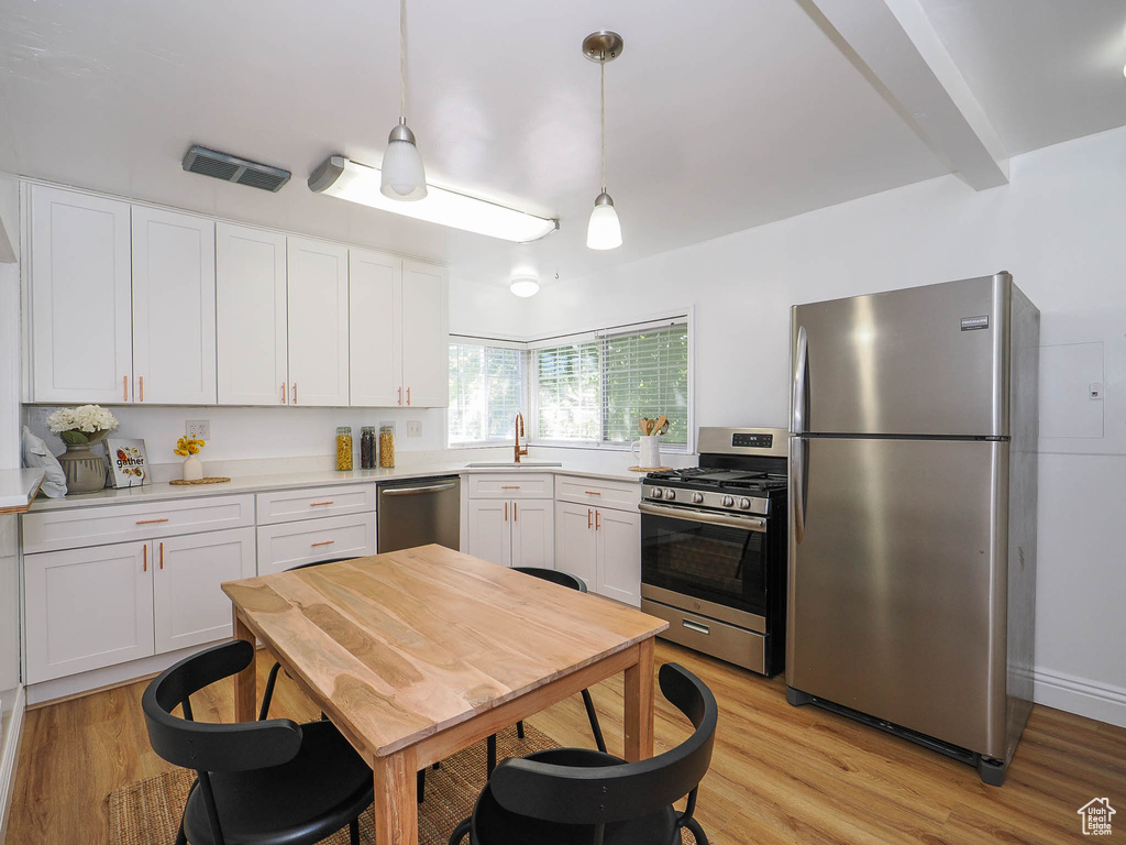 Kitchen with appliances with stainless steel finishes, light countertops, pendant lighting, and white cabinets