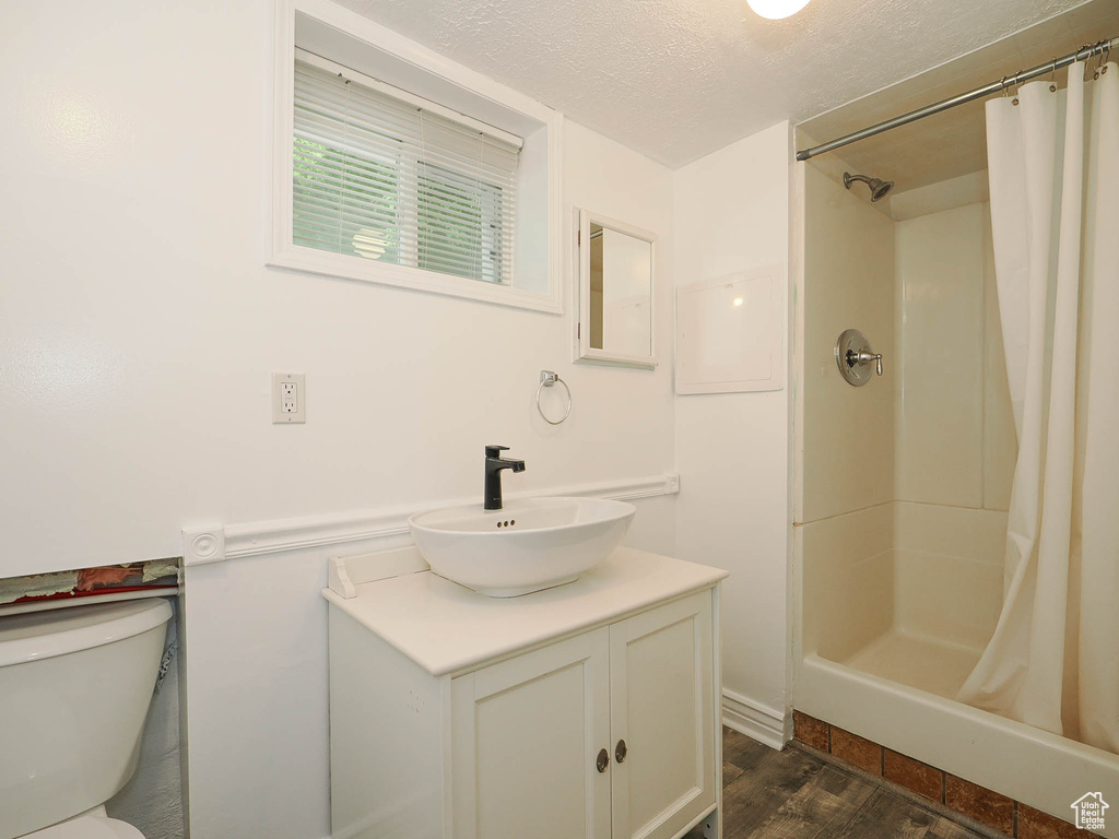 Bathroom featuring a textured ceiling, toilet, wood finished floors, vanity, and a shower stall