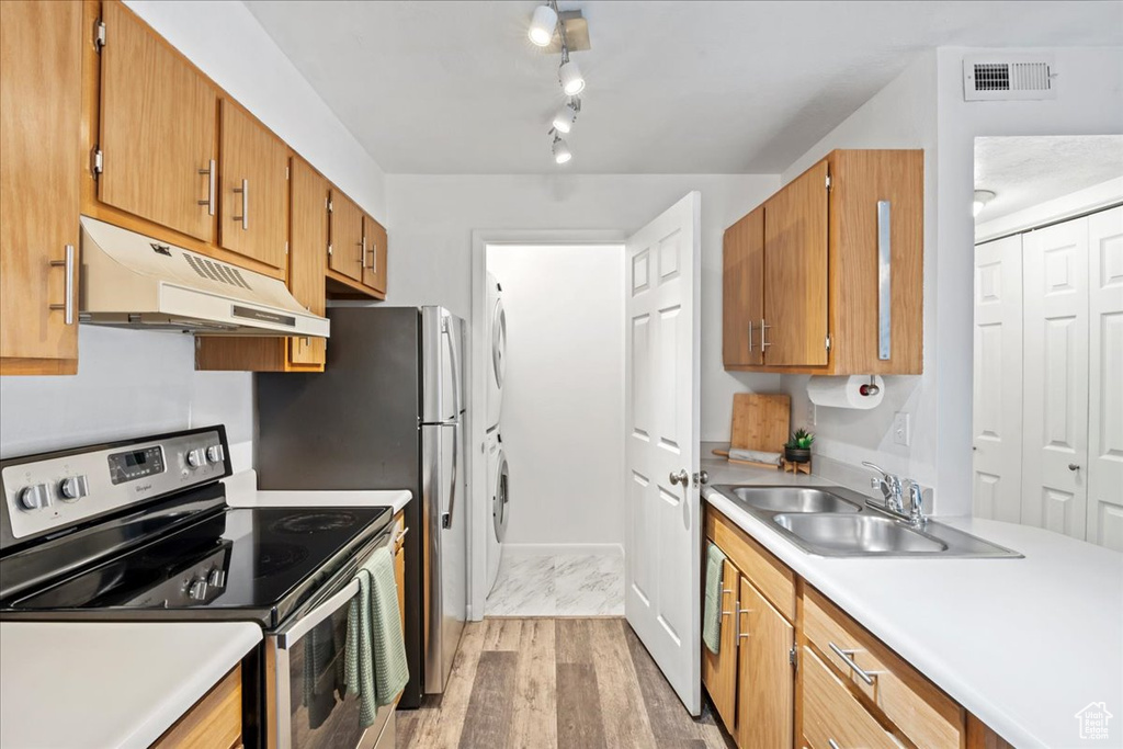 Kitchen with electric stove, light countertops, stacked washer and clothes dryer, and under cabinet range hood