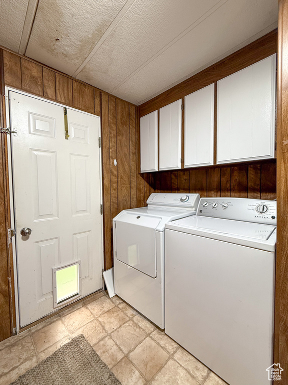 Clothes washing area featuring cabinet space, stone finish floor, washer and clothes dryer, and wood walls