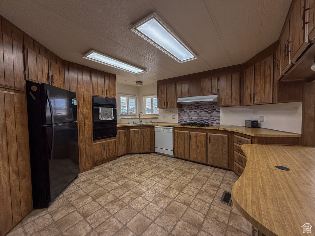 Kitchen with light countertops, a warming drawer, under cabinet range hood, and black appliances