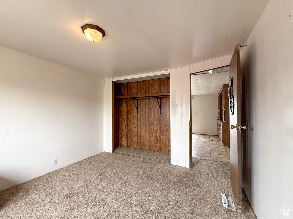 Unfurnished bedroom featuring light carpet, wood walls, and a closet