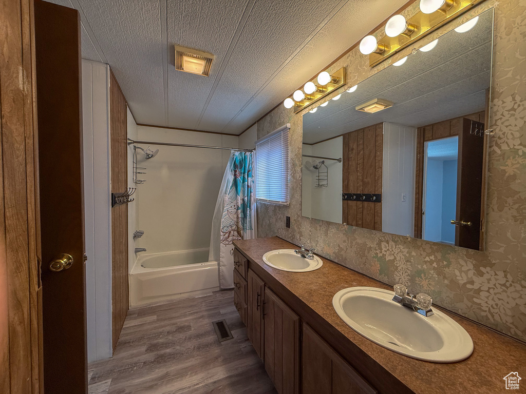 Bathroom with shower / bath combination with curtain, a sink, a textured ceiling, and wood finished floors