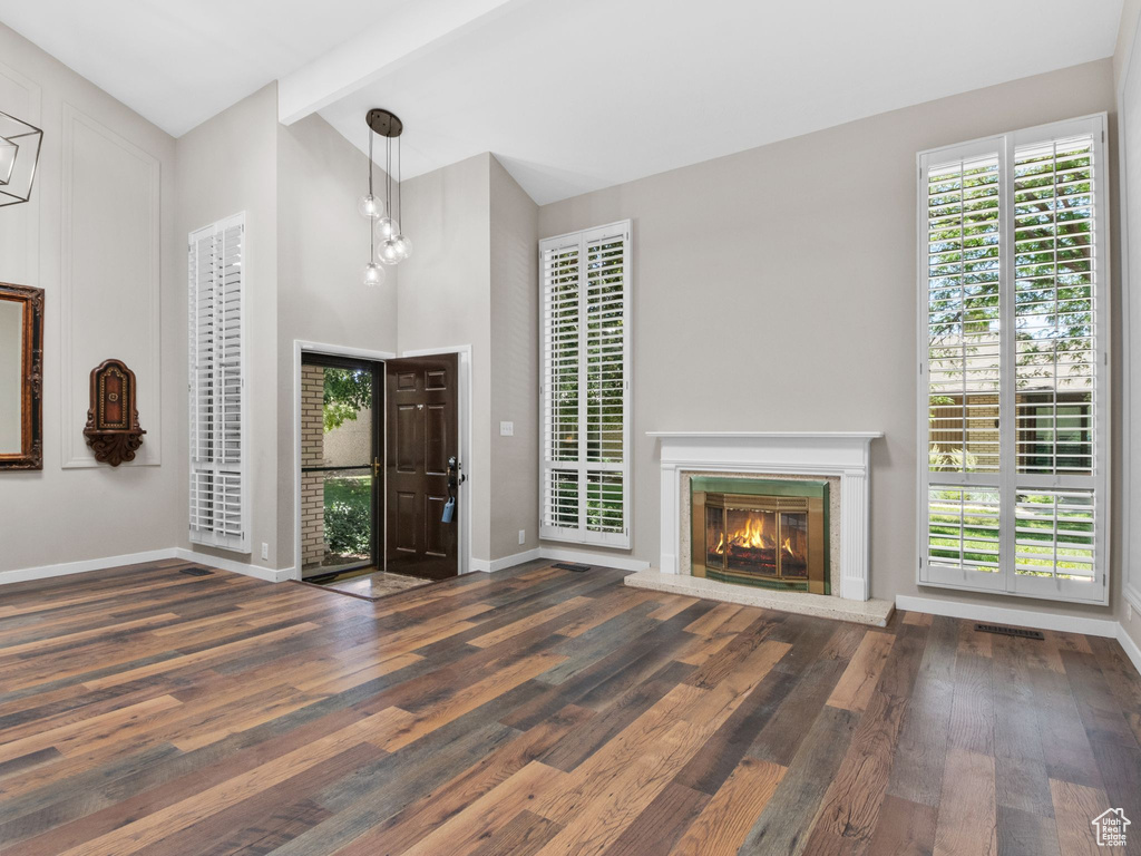 Entrance foyer with wood finished floors, beam ceiling, a glass covered fireplace, and high vaulted ceiling
