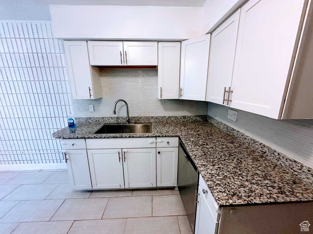 Kitchen with tasteful backsplash, dishwashing machine, dark stone countertops, white cabinetry, and a sink