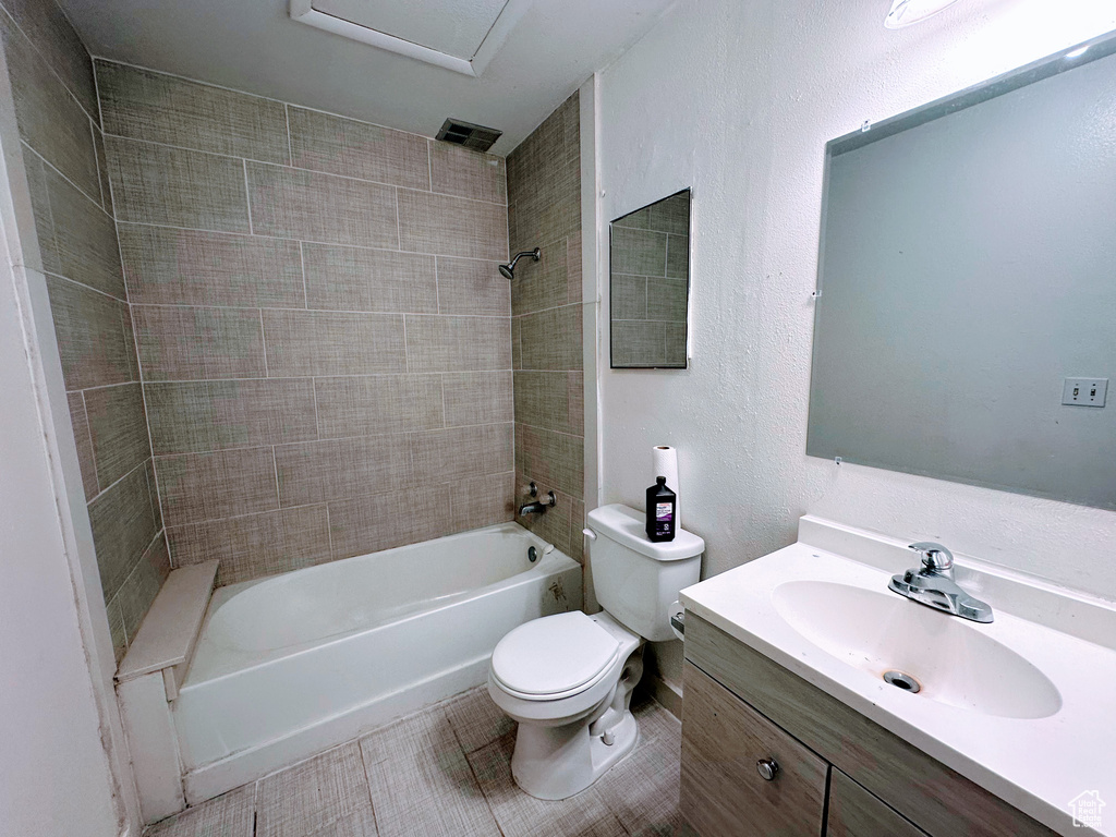 Bathroom featuring a textured wall, toilet, vanity, tile patterned floors, and washtub / shower combination
