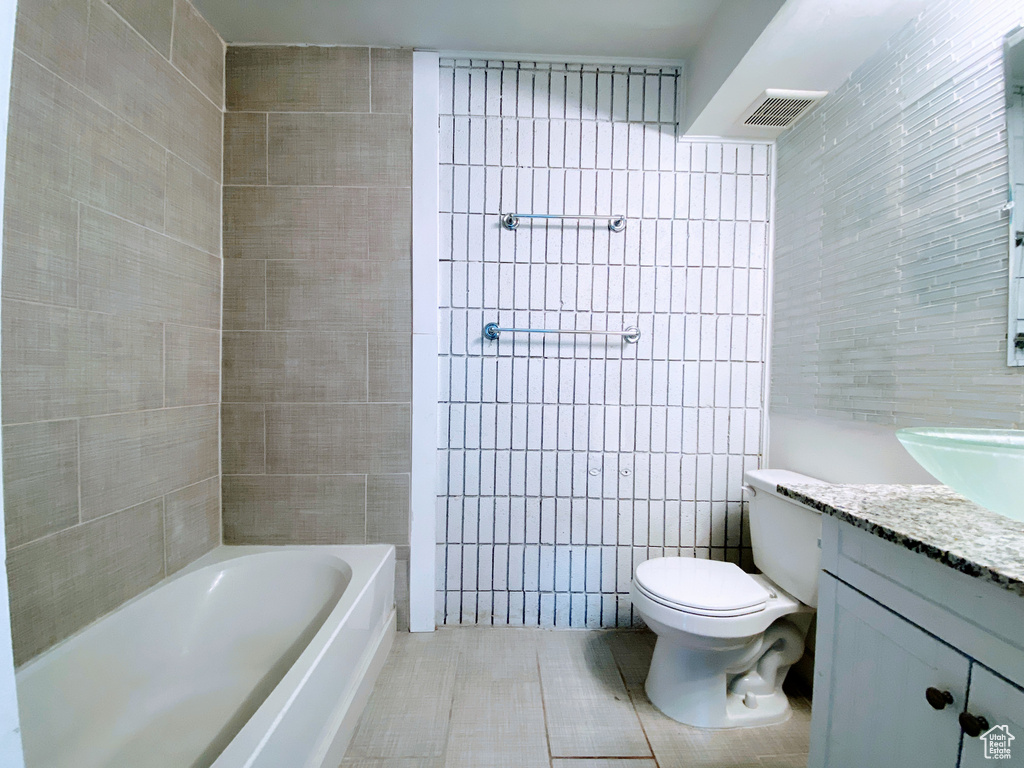 Bathroom featuring tile patterned flooring, toilet, a bathing tub, vanity, and tile walls