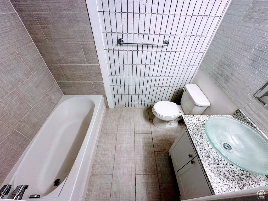 Bathroom featuring a tub to relax in, tile walls, toilet, vanity, and tile patterned flooring