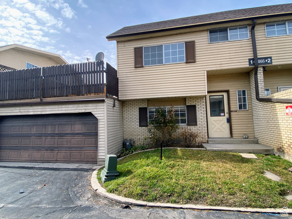 View of property featuring a garage, driveway, a front yard, and brick siding