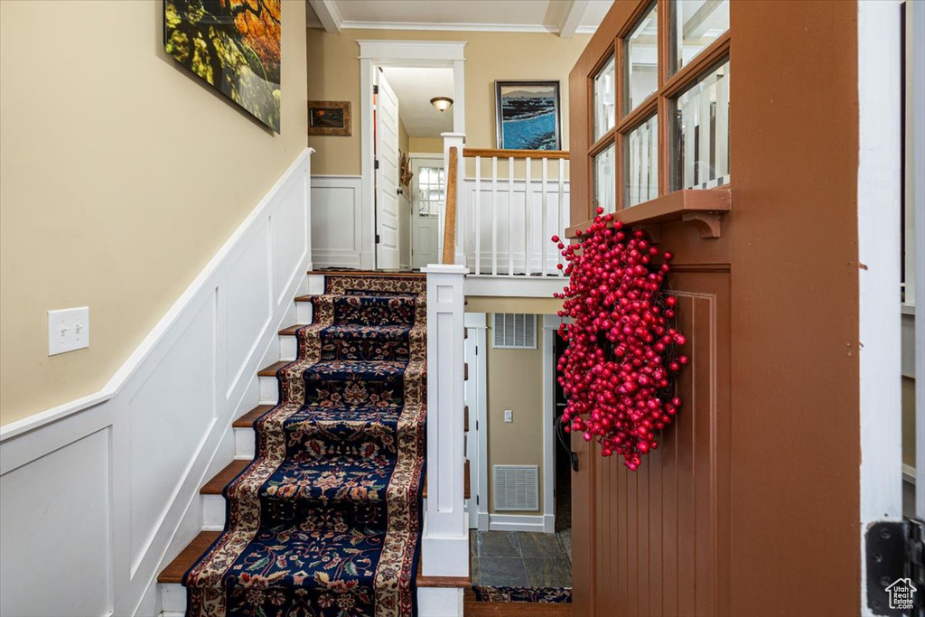 Staircase featuring a wainscoted wall, visible vents, ornamental molding, and a decorative wall