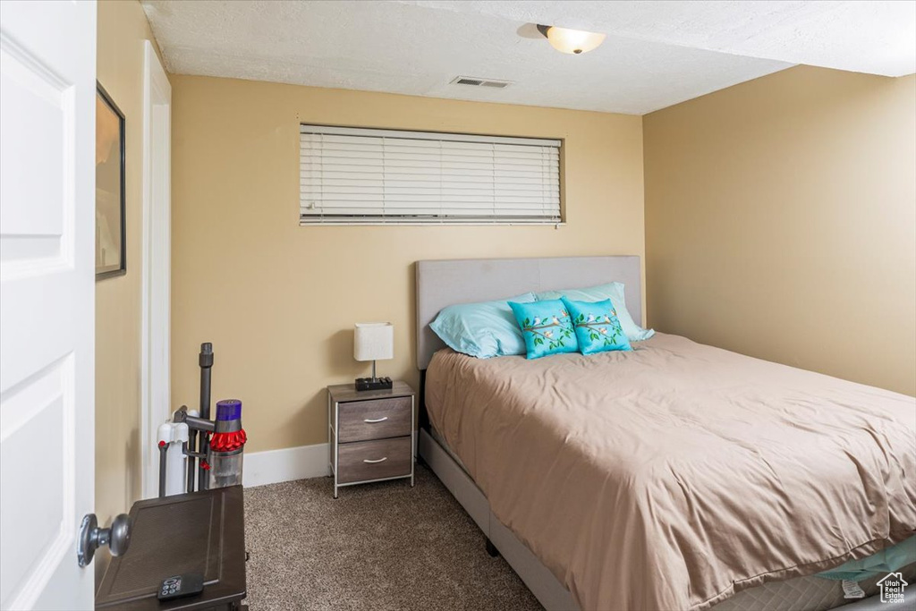 Bedroom featuring a textured ceiling, dark colored carpet, visible vents, and baseboards