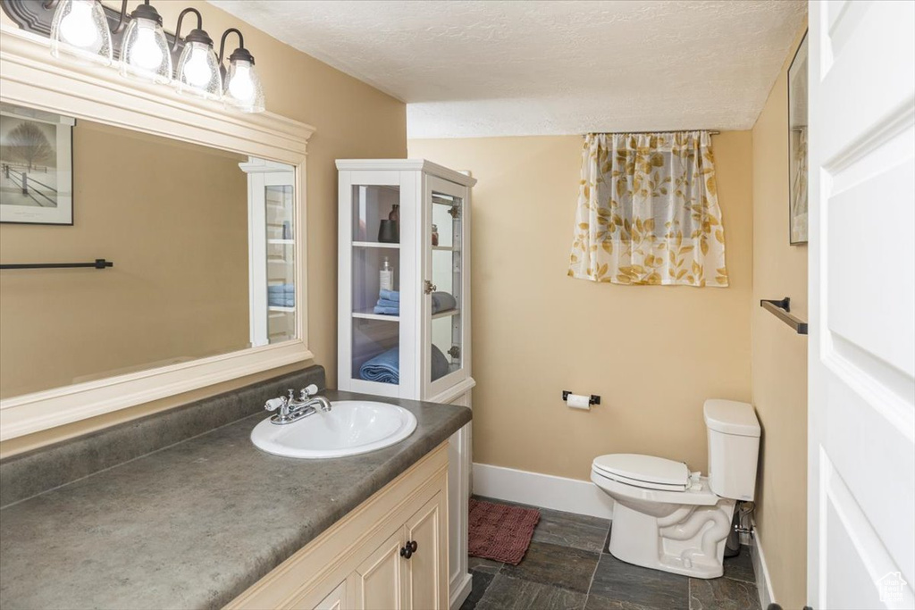 Bathroom featuring toilet, a textured ceiling, vanity, and baseboards
