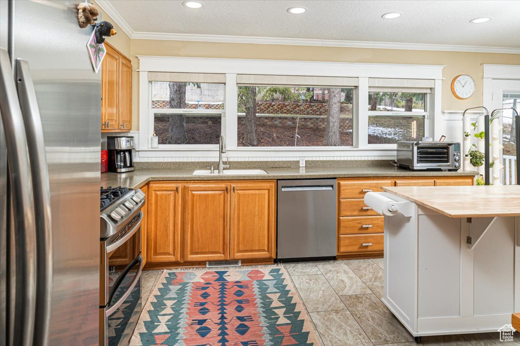Kitchen featuring a toaster, stainless steel appliances, a sink, brown cabinets, and crown molding