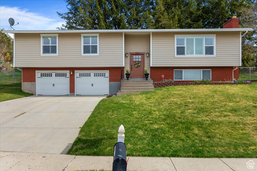 Split foyer home with a front yard, brick siding, an attached garage, a chimney, and concrete driveway