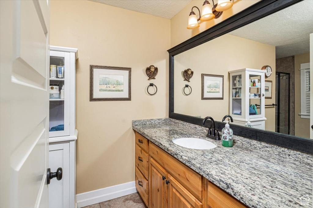 Full bathroom featuring an enclosed shower, baseboards, a textured ceiling, and vanity