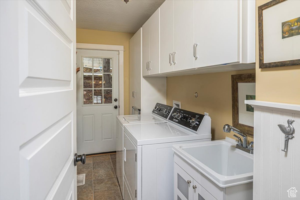 Laundry room with cabinet space, a textured ceiling, washer and clothes dryer, and a sink