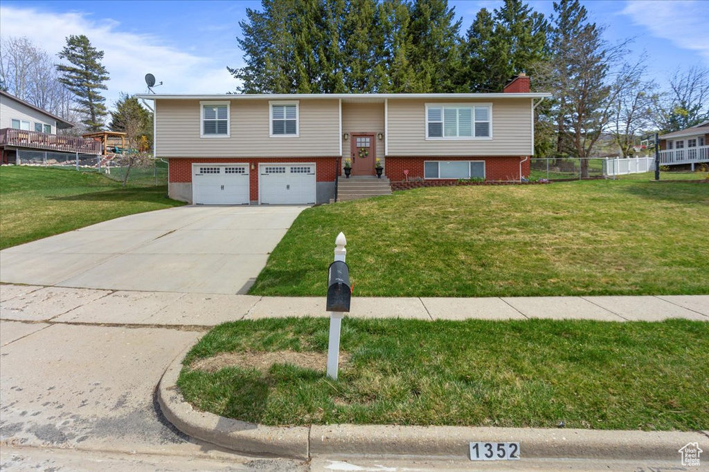Raised ranch with a front yard, a garage, a chimney, fence, and driveway