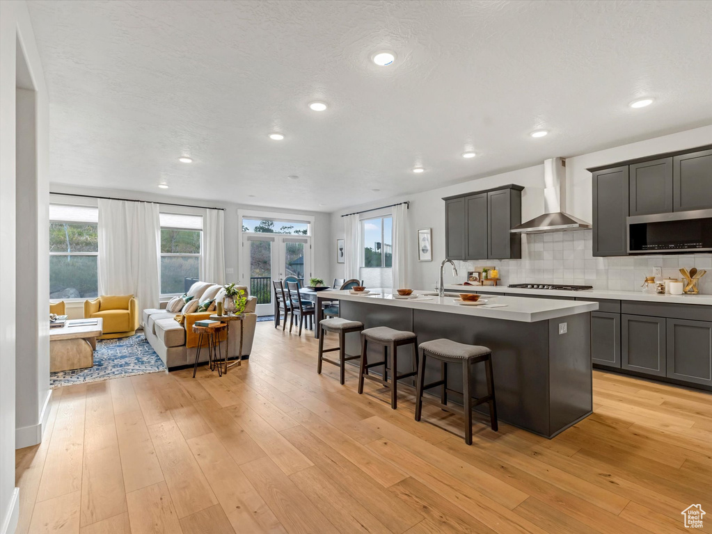 Kitchen with wall chimney range hood, stainless steel microwave, gas stovetop, a kitchen bar, and a kitchen island with sink