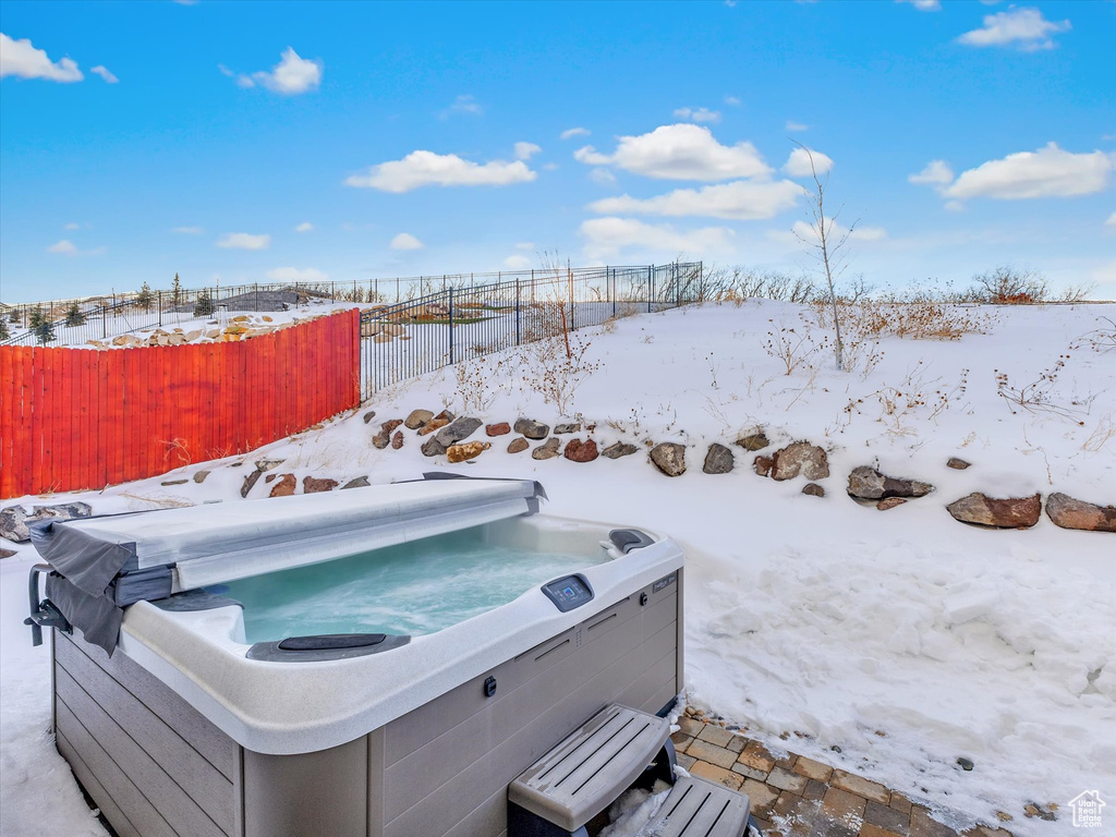 Yard covered in snow featuring fence and a hot tub