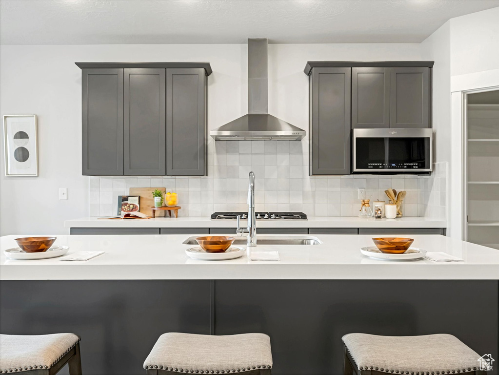 Kitchen featuring wall chimney range hood, stainless steel microwave, tasteful backsplash, and light countertops