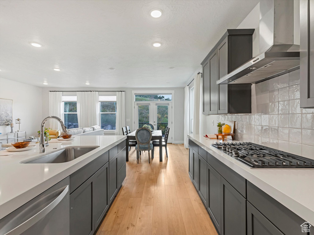 Kitchen featuring wall chimney range hood, stainless steel appliances, french doors, light countertops, and recessed lighting