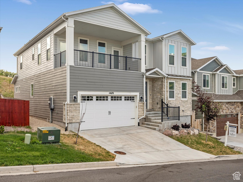 View of front of house featuring a balcony, stone siding, driveway, an attached garage, and board and batten siding